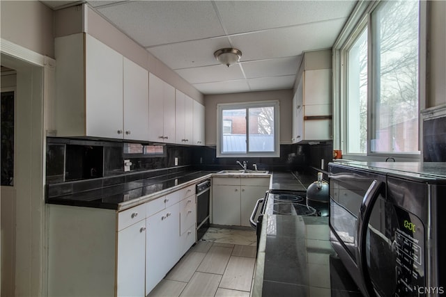 kitchen featuring sink, a drop ceiling, backsplash, white cabinetry, and light tile flooring