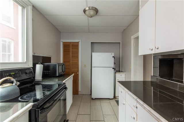 kitchen with white refrigerator, a drop ceiling, white cabinets, and black electric range oven