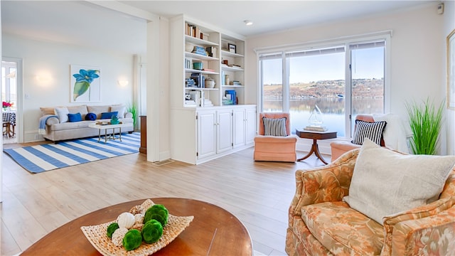 living room with a water view, built in features, and light hardwood / wood-style flooring