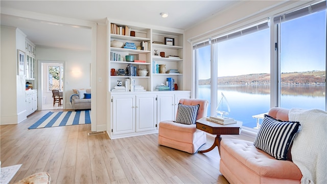 sitting room featuring built in shelves, a water view, light wood-type flooring, and ornamental molding