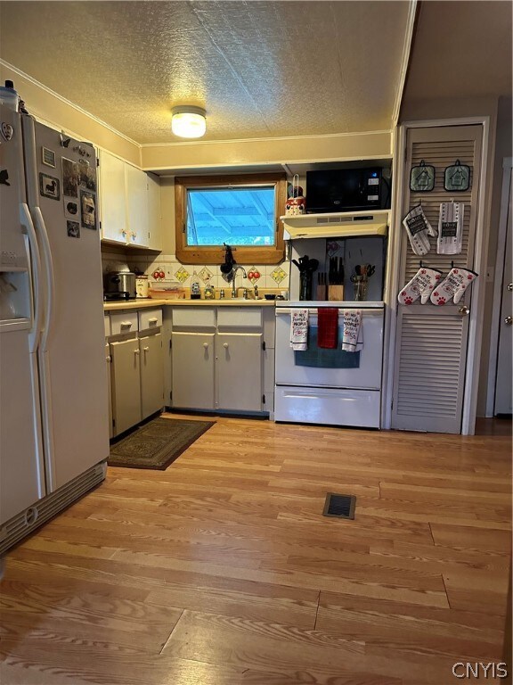 kitchen featuring white refrigerator, a textured ceiling, range, black microwave, and light wood-type flooring