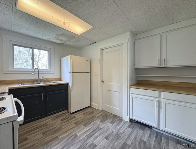 kitchen with stove, white cabinetry, a drop ceiling, white fridge, and sink