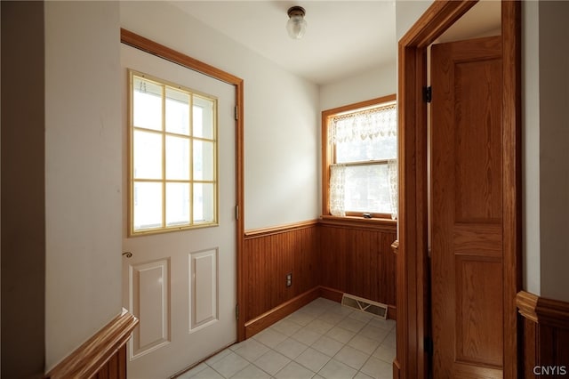 doorway with wooden walls and light tile patterned floors