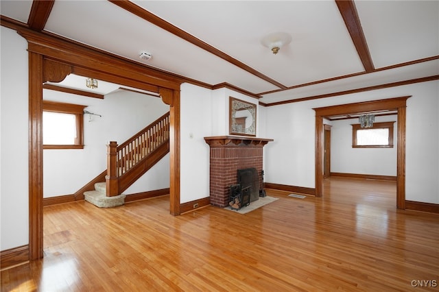 unfurnished living room featuring ornamental molding, a healthy amount of sunlight, light wood-type flooring, and a brick fireplace