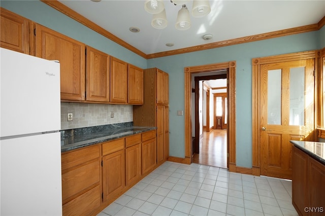 kitchen featuring white fridge, crown molding, dark stone countertops, and plenty of natural light