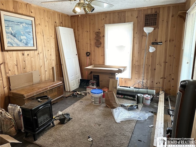 miscellaneous room with ceiling fan, wooden walls, a wood stove, and a textured ceiling