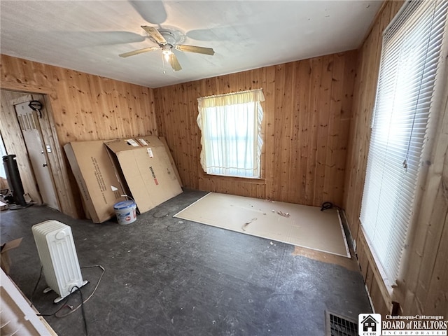 spare room featuring ceiling fan, radiator, and wooden walls