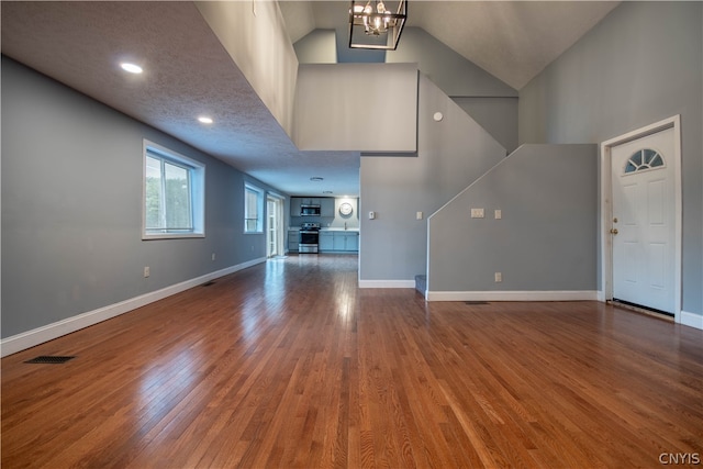 unfurnished living room featuring a notable chandelier, a towering ceiling, and hardwood / wood-style flooring