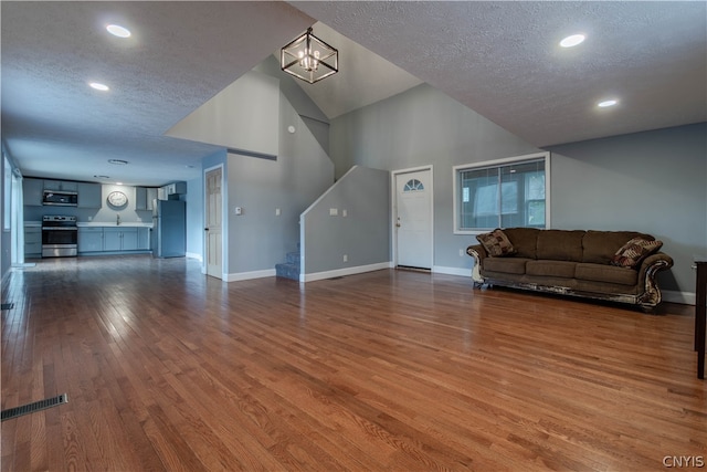 living room featuring a textured ceiling, an inviting chandelier, dark hardwood / wood-style flooring, a towering ceiling, and sink