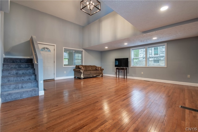 unfurnished living room featuring a textured ceiling, hardwood / wood-style flooring, a chandelier, a healthy amount of sunlight, and a towering ceiling