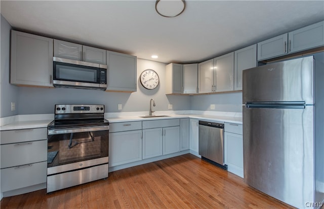 kitchen with appliances with stainless steel finishes, sink, and light hardwood / wood-style flooring