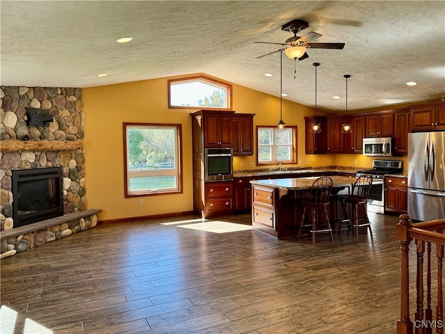 kitchen with appliances with stainless steel finishes, vaulted ceiling, dark wood-type flooring, a kitchen island, and a kitchen bar