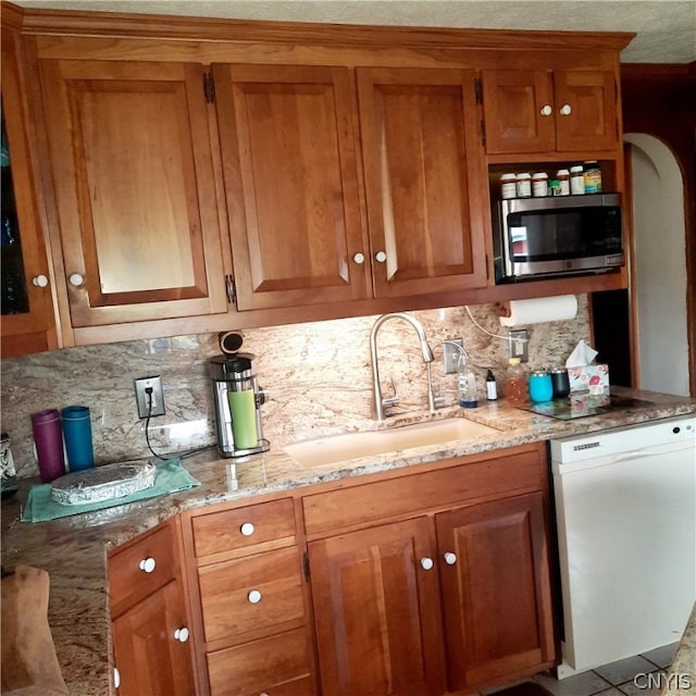 kitchen featuring light stone countertops, backsplash, white dishwasher, and sink