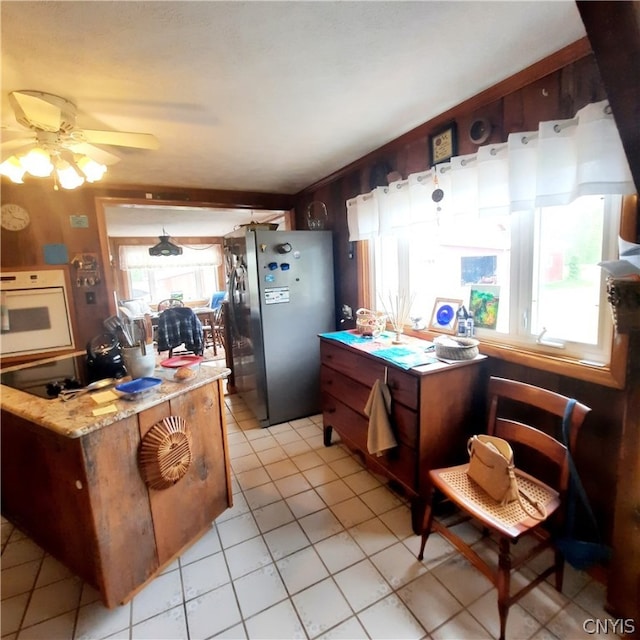 kitchen with oven, stainless steel fridge, light tile patterned floors, ceiling fan, and dark brown cabinetry