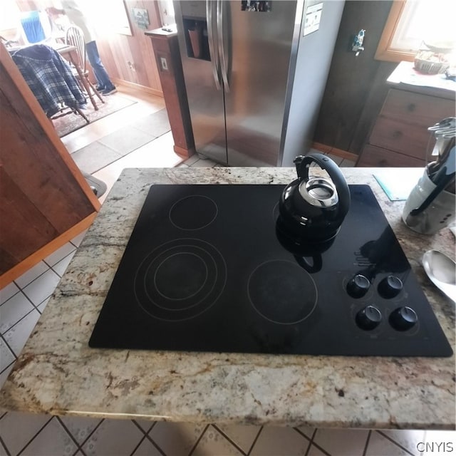 kitchen featuring black electric stovetop, light tile patterned flooring, and stainless steel fridge