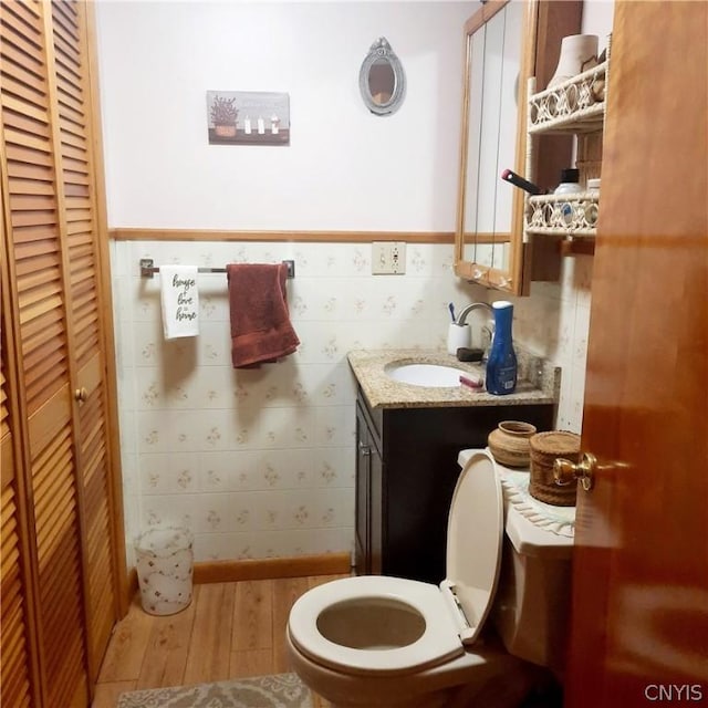 bathroom with a wainscoted wall, toilet, wood finished floors, and a closet