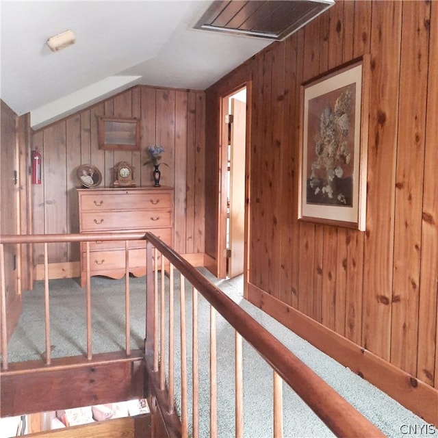 hallway with lofted ceiling, carpet floors, and wooden walls