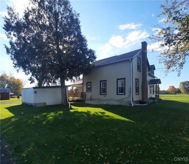 rear view of property featuring a wooden deck, a chimney, and a yard