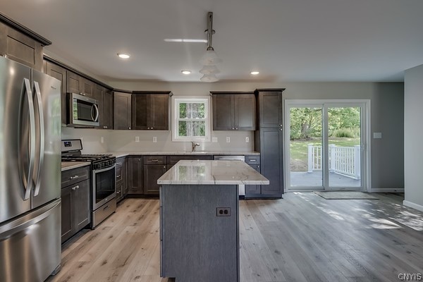 kitchen with appliances with stainless steel finishes, a healthy amount of sunlight, a center island, and light hardwood / wood-style flooring