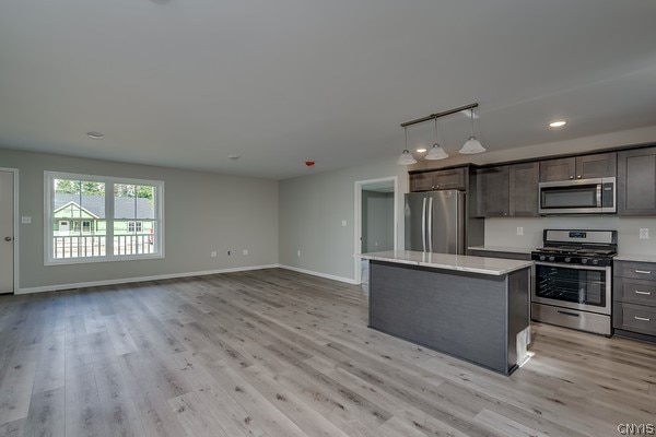 kitchen featuring stainless steel appliances, pendant lighting, light wood-type flooring, and a kitchen island