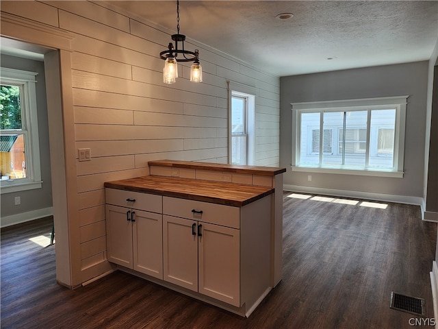 kitchen featuring butcher block counters, dark wood-type flooring, a textured ceiling, hanging light fixtures, and wood walls