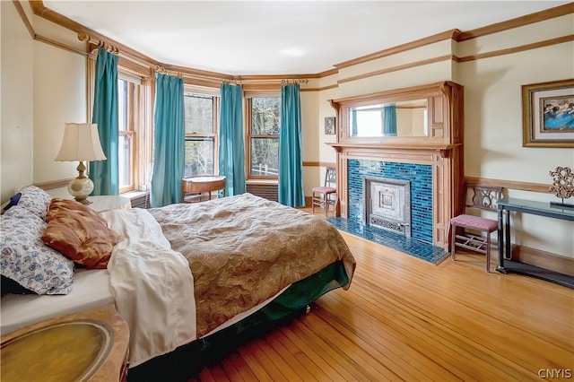 bedroom with ornamental molding, wood-type flooring, and a fireplace