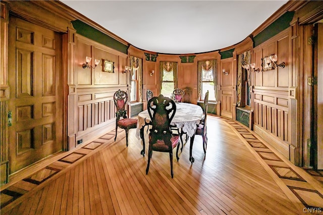 dining room with ornamental molding, wooden walls, and light hardwood / wood-style flooring