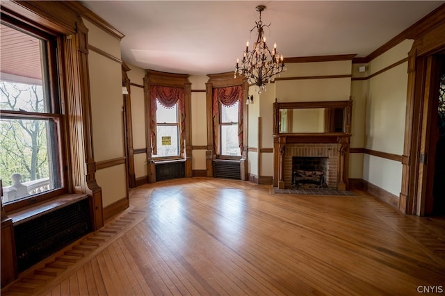 unfurnished living room with hardwood / wood-style flooring, ornamental molding, a brick fireplace, an inviting chandelier, and radiator heating unit