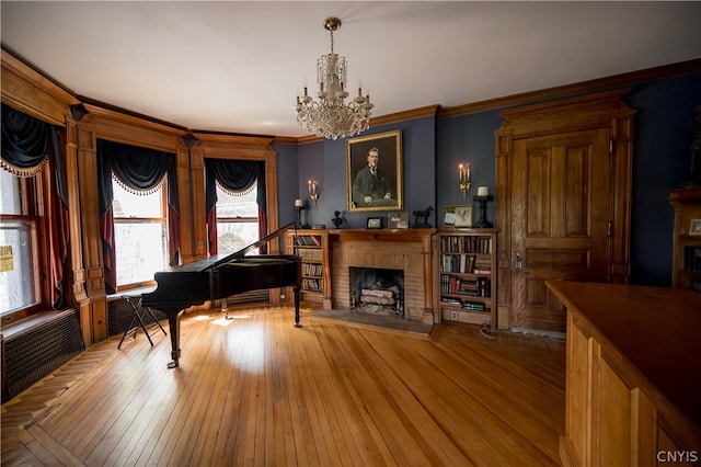 living area with ornamental molding, a chandelier, a brick fireplace, and hardwood / wood-style flooring