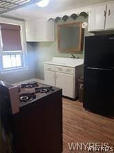 kitchen featuring black refrigerator, gas stove, sink, hardwood / wood-style flooring, and white cabinets