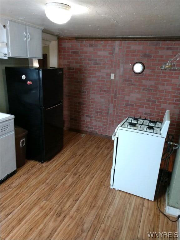 kitchen with white cabinets, black refrigerator, light wood-type flooring, white gas range, and brick wall