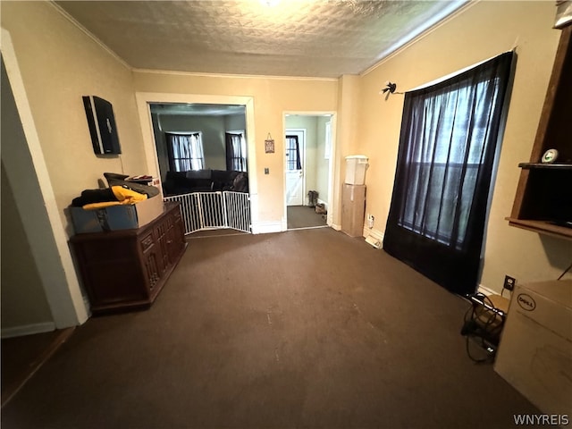 hallway with a textured ceiling, ornamental molding, and dark carpet