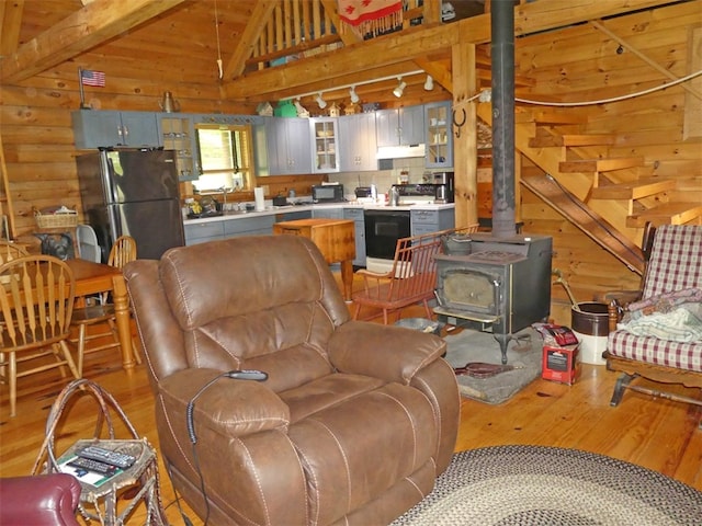 living room with light hardwood / wood-style floors, wooden walls, lofted ceiling with beams, and a wood stove