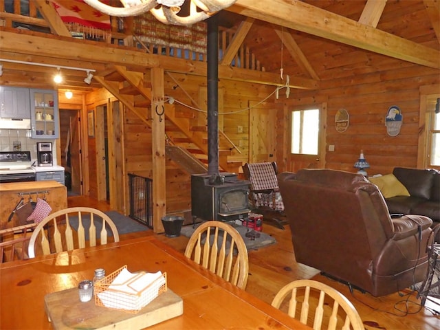 dining area featuring vaulted ceiling with beams, hardwood / wood-style floors, wooden walls, and a wood stove