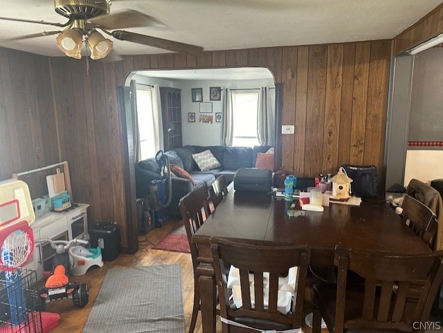 dining room with wood-type flooring, wooden walls, and ceiling fan