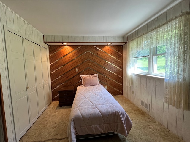 bedroom with light colored carpet, wooden walls, and a closet