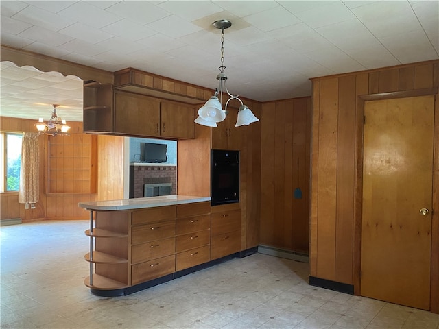 kitchen featuring black oven, wood walls, kitchen peninsula, and decorative light fixtures