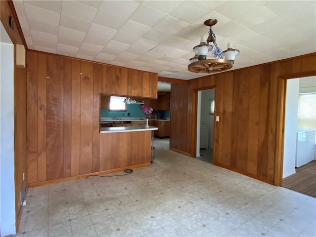 kitchen with washer / clothes dryer, kitchen peninsula, hanging light fixtures, and wooden walls