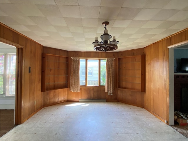 spare room with baseboard heating, wooden walls, and a chandelier