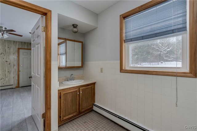 bathroom with a baseboard radiator, tile walls, vanity, and ceiling fan