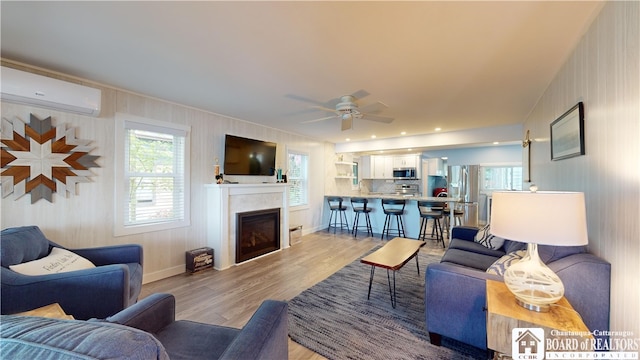 living room with a wall unit AC, ceiling fan, a high end fireplace, and light wood-type flooring