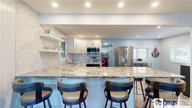 kitchen featuring stainless steel appliances, tasteful backsplash, a kitchen bar, light stone countertops, and white cabinets