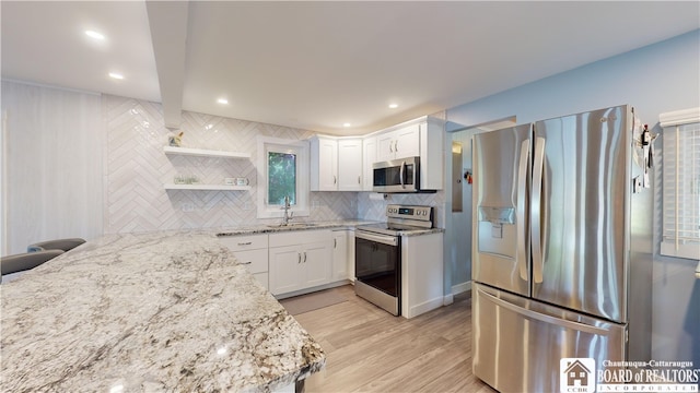 kitchen with backsplash, appliances with stainless steel finishes, white cabinetry, and light wood-type flooring