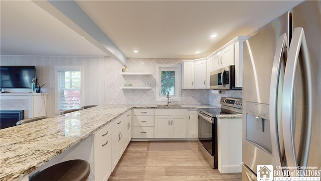 kitchen with stainless steel appliances, white cabinetry, backsplash, and light stone countertops