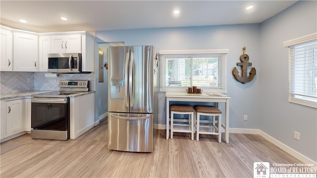 kitchen with light hardwood / wood-style flooring, backsplash, light stone countertops, white cabinets, and appliances with stainless steel finishes