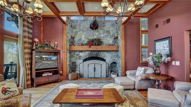 living room featuring light wood-type flooring, coffered ceiling, beamed ceiling, a chandelier, and a stone fireplace