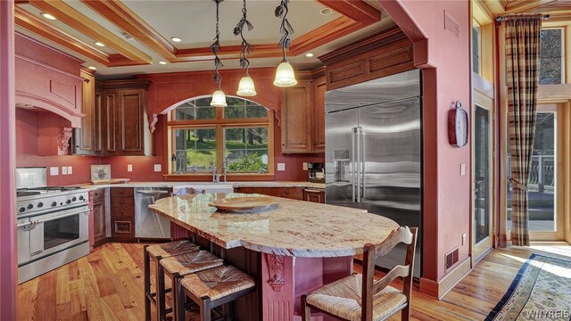 kitchen with light stone countertops, premium appliances, light hardwood / wood-style floors, pendant lighting, and a kitchen bar