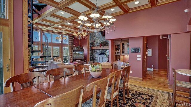 dining area with a high ceiling, coffered ceiling, an inviting chandelier, a stone fireplace, and beamed ceiling