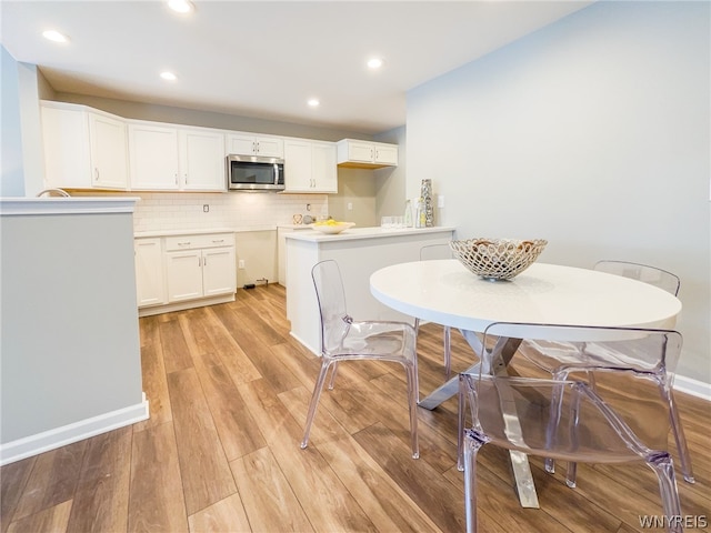 kitchen featuring white cabinets, light wood-type flooring, kitchen peninsula, and backsplash