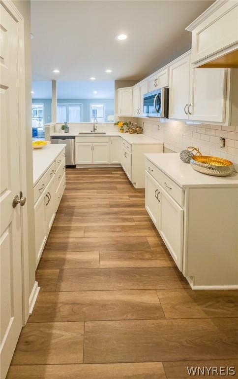 202 Carriage Ln, West Seneca, NY 14224 - kitchen featuring appliances with stainless steel finishes, light wood-style flooring, a sink, white cabinets, and light countertops